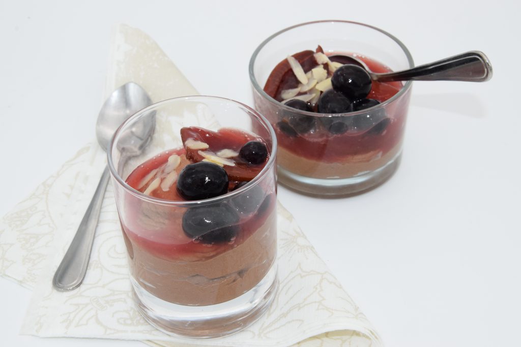 Zwei Gläser mit Schokomousse mit Weinbrand, Zwetschgen und Trauben. Neben dem vorderen Glas liegt ein kleiner Dessertlöffel auf einer weißen Stoffserviette.